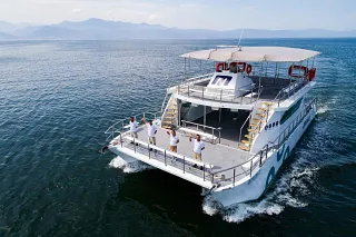 Vista aérea del Catamaran 72 navegando con tripulantes en la proa sobre el mar azul