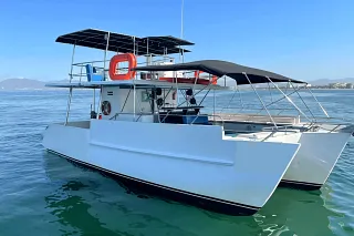 The Custom 34 Trimaran at anchor on calm water, with its two-level canopy and mountains beyond
