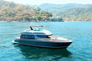 The Custom 60 anchored in turquoise water below jungle-covered hills dotted with houses