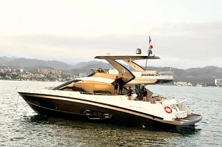 El Custom 70 en el agua con invitados en la popa, frente a la costa y montañas