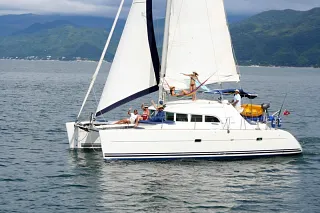 El catamarán Lagoon 38 navegando a vela con invitados a bordo y montañas verdes al fondo