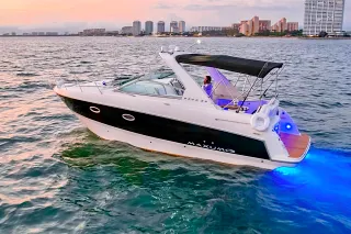The Maxum 30 cruising at dusk with blue underwater lights in front of apartment towers