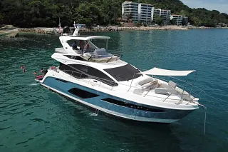 El Sea Ray 55 anclado en aguas verdes junto a un cerro con edificios y bañistas cerca