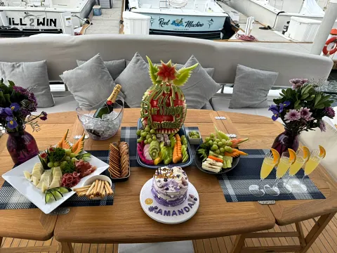 An aft-deck table on a yacht set with cheese, fruit, flowers and a birthday cake