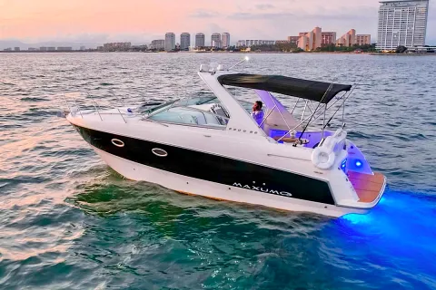 Yate navegando al atardecer con luces de la ciudad encendidas en la costa