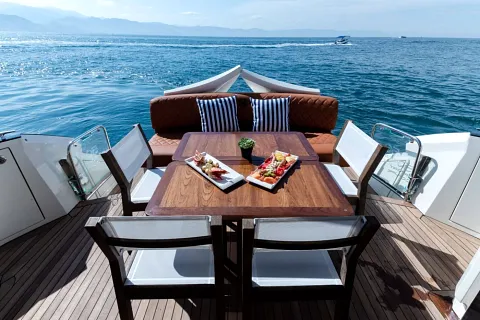 Mesa de teca con charolas de botanas en la cubierta de un yate, con el mar de fondo